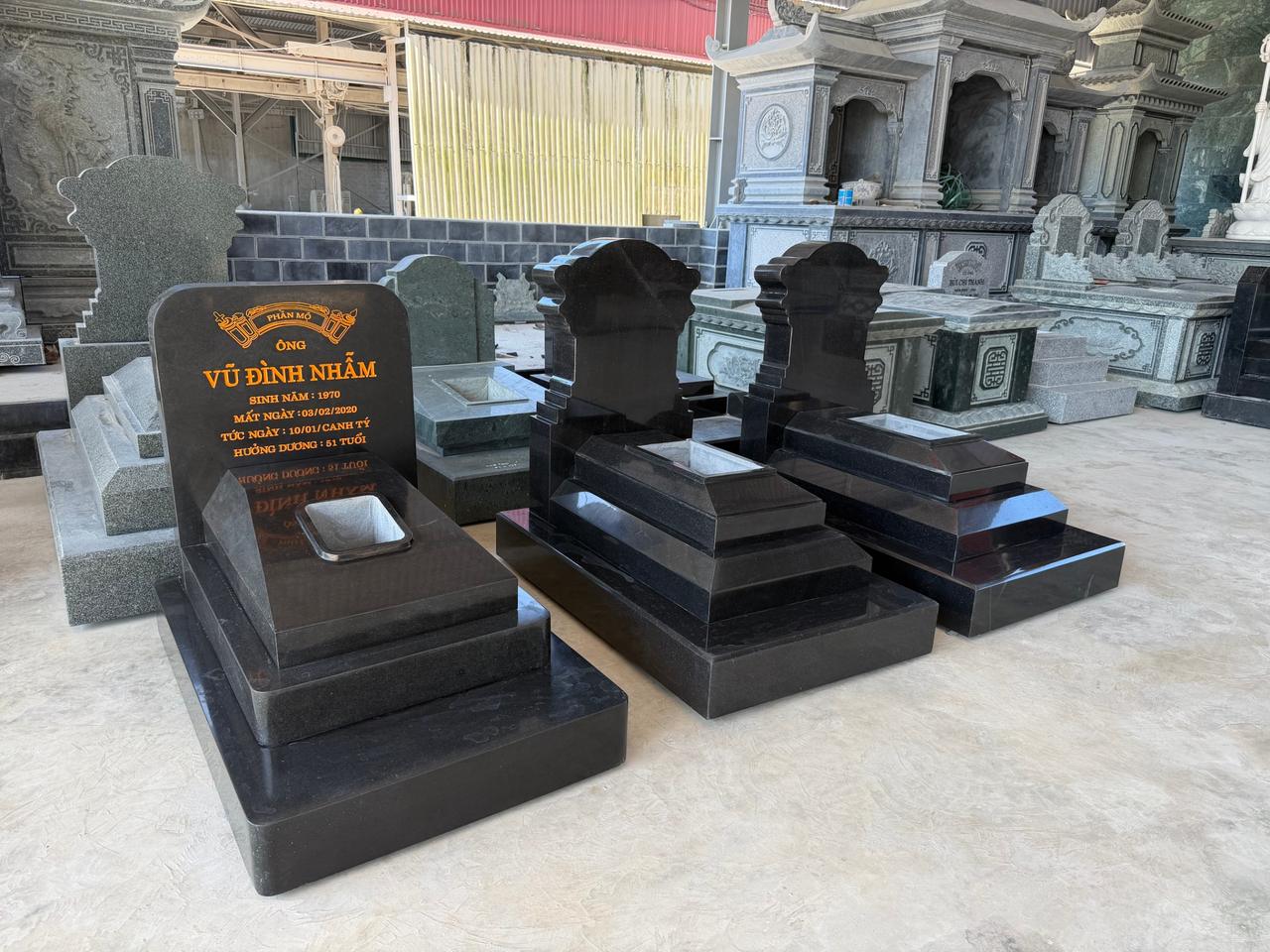 Mộ Đá Đơn: Sản Phẩm Bán Chạy Nhất, Mẫu Đẹp 2026 7 Mộ đơn granite đen đặt cạnh sản phẩm đá xanh rêu tại xưởng Quang Trung, thấy rõ khác biệt hai chất liệu
