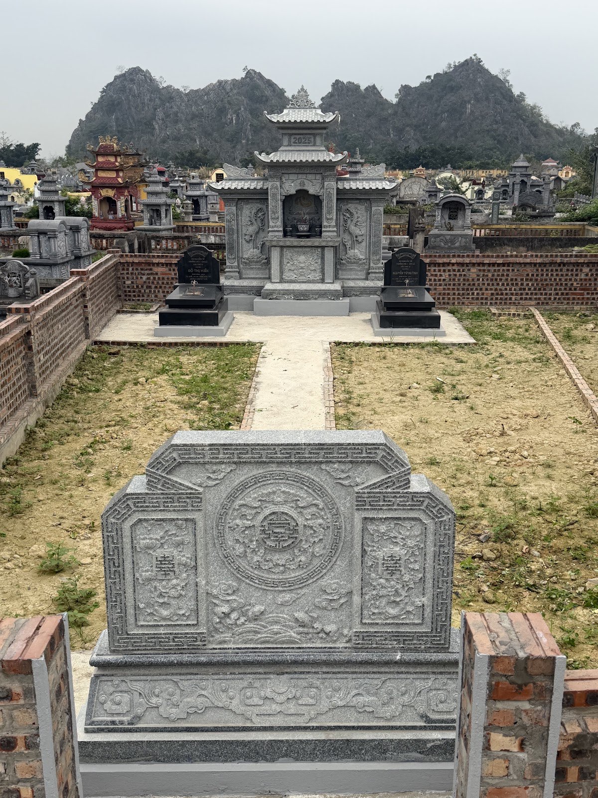 Cuốn thư đá vuông đặt ở lối vào khuôn viên gia đình, phía sau là lăng thờ và hai ngôi mộ trên cùng trục