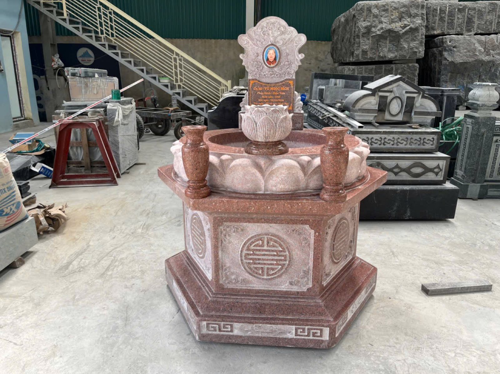 Mộ lục giác granite đỏ có bát sen, hai lọ hoa và bia ảnh, đặt trong xưởng Quang Trung trước khi giao